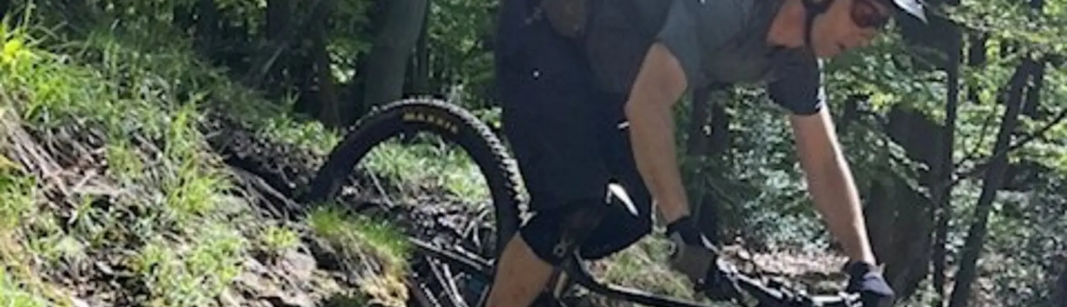 Ein Mountainbiker mit Helm und Rucksack fährt steil bergab durch einen sonnigen Waldabschnitt. | © DAV Dortmund