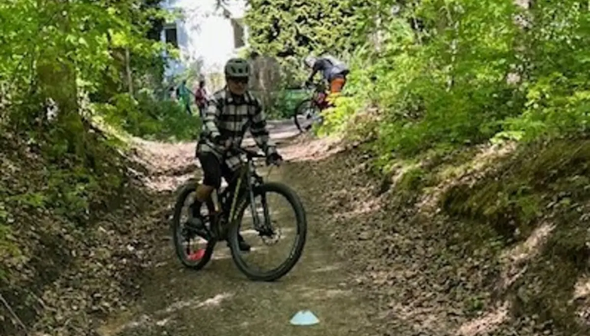 Kind fährt mit einem Mountainbike durch einen markierten Übungsparcours auf einem Waldweg, im Hintergrund eine Hütte. | © DAV Dortmund