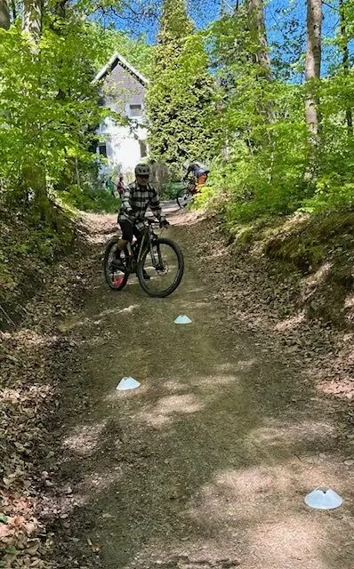 Kind fährt mit einem Mountainbike durch einen markierten Übungsparcours auf einem Waldweg, im Hintergrund eine Hütte. | © DAV Dortmund