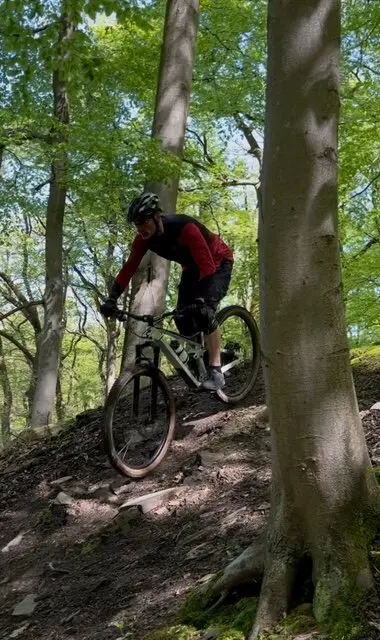 Person fährt mit Helm und Schutzkleidung auf einem steilen Trail zwischen Bäumen bergab. | © DAV Dortmund