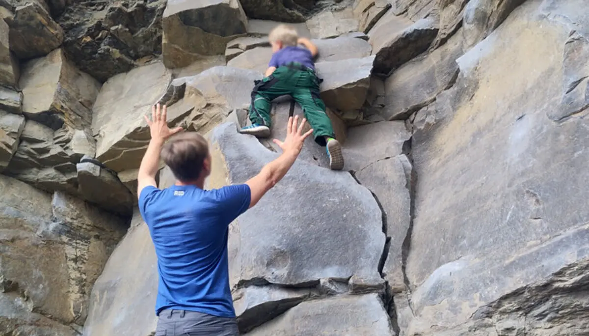 Ein Erwachsener sichert ein Kind, das in einer Felswand klettert. Beide befinden sich im unteren Bereich der Route. | © DAV Dortmund