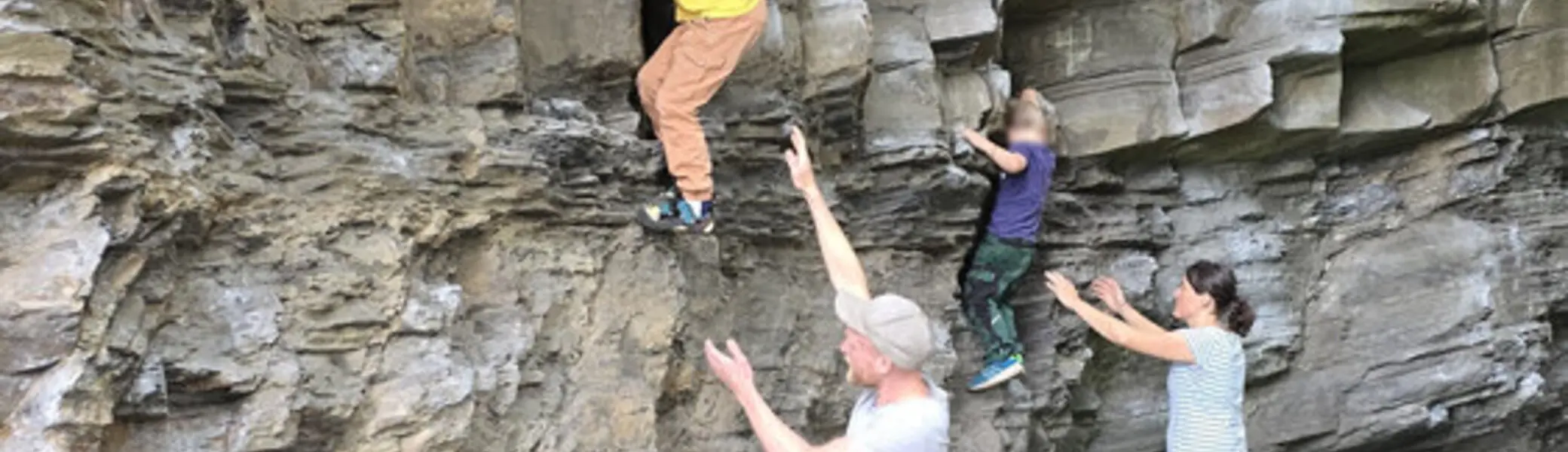 Zwei Kinder klettern nebeneinander an einer Felswand, während drei Erwachsene sie sichern und ein Crashpad am Boden liegt. | © DAV Dortmund