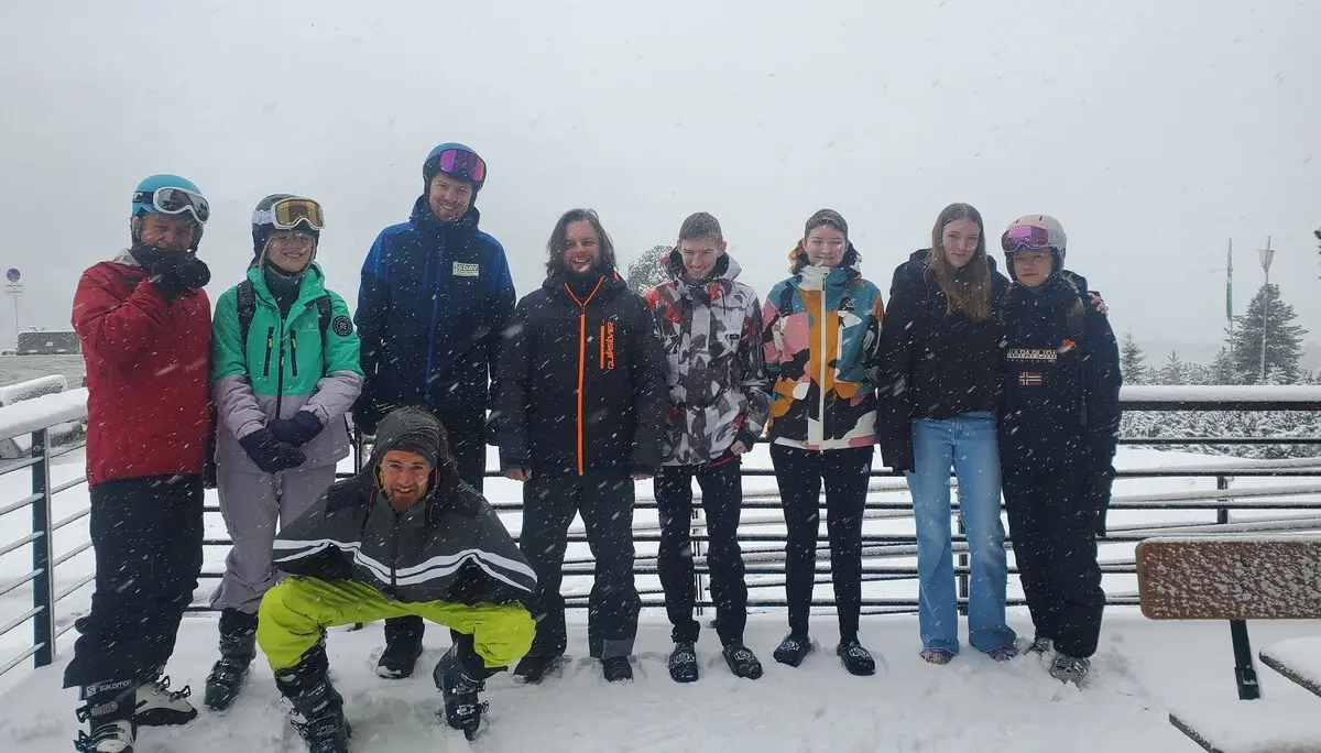 Neun junge Menschen stehen auf einer verschneiten Terrasse, eine Person hockt vorne – alle in Winterkleidung. | © DAV Dortmund