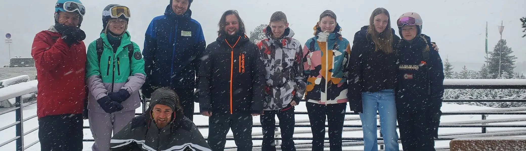 Neun junge Menschen stehen auf einer verschneiten Terrasse, eine Person hockt vorne – alle in Winterkleidung. | © DAV Dortmund