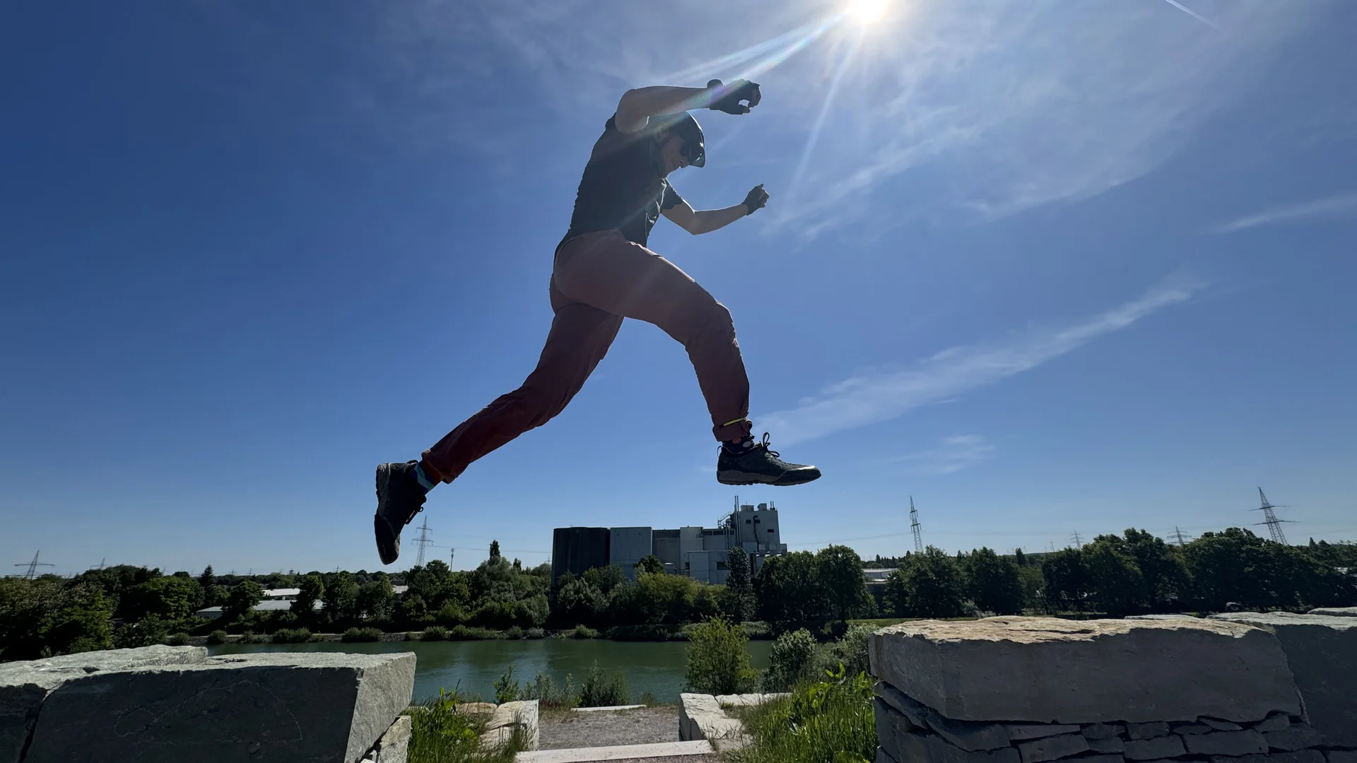 Person springt bei Sonnenschein über eine Mauer mit Stadtlandschaft im Hintergrund. | © DAV Dortmund