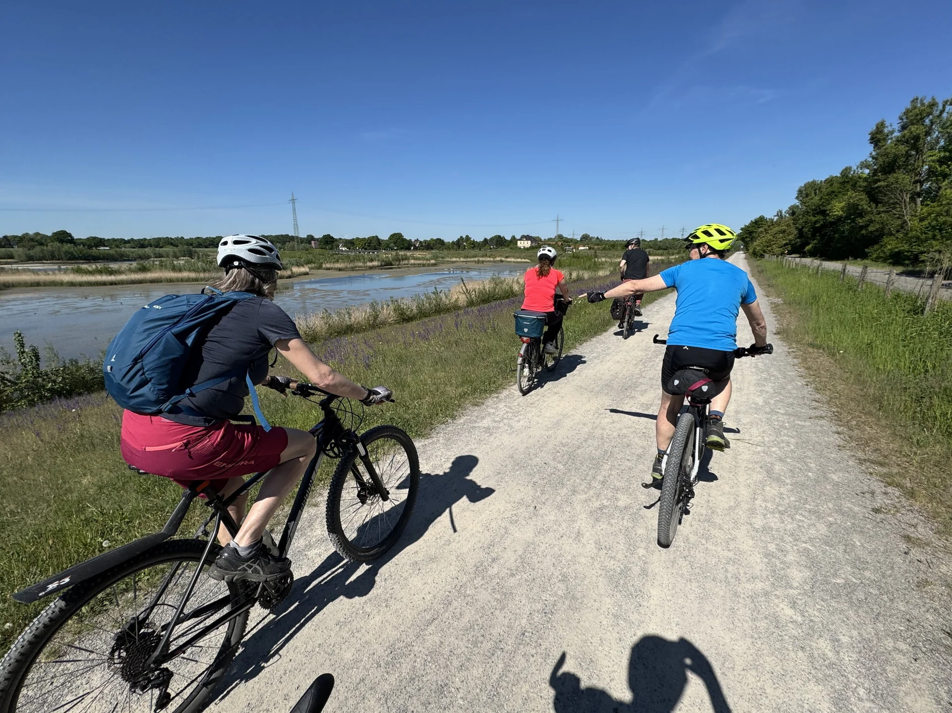 Mehrere Radfahrer*innen fahren bei Sonnenschein auf einem breiten Schotterweg neben einem Gewässer. | © DAV Dortmund