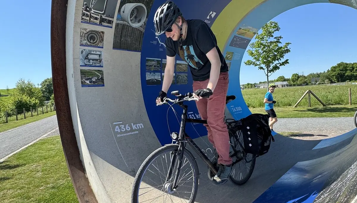 Mann fährt mit Fahrrad durch ein großes, rundes Kunstobjekt im Freien. | © DAV Dortmund