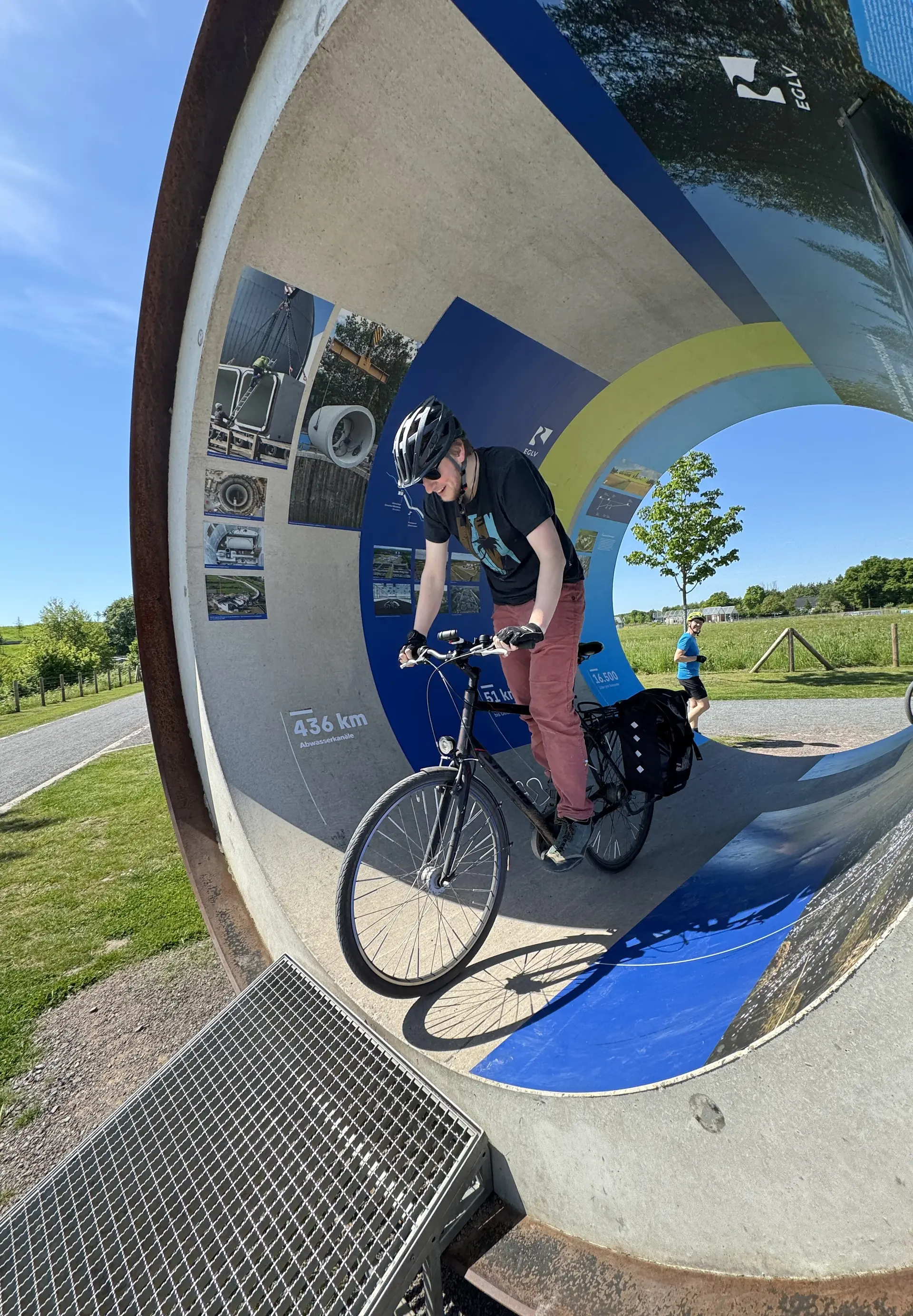 Mann fährt mit Fahrrad durch ein großes, rundes Kunstobjekt im Freien. | © DAV Dortmund