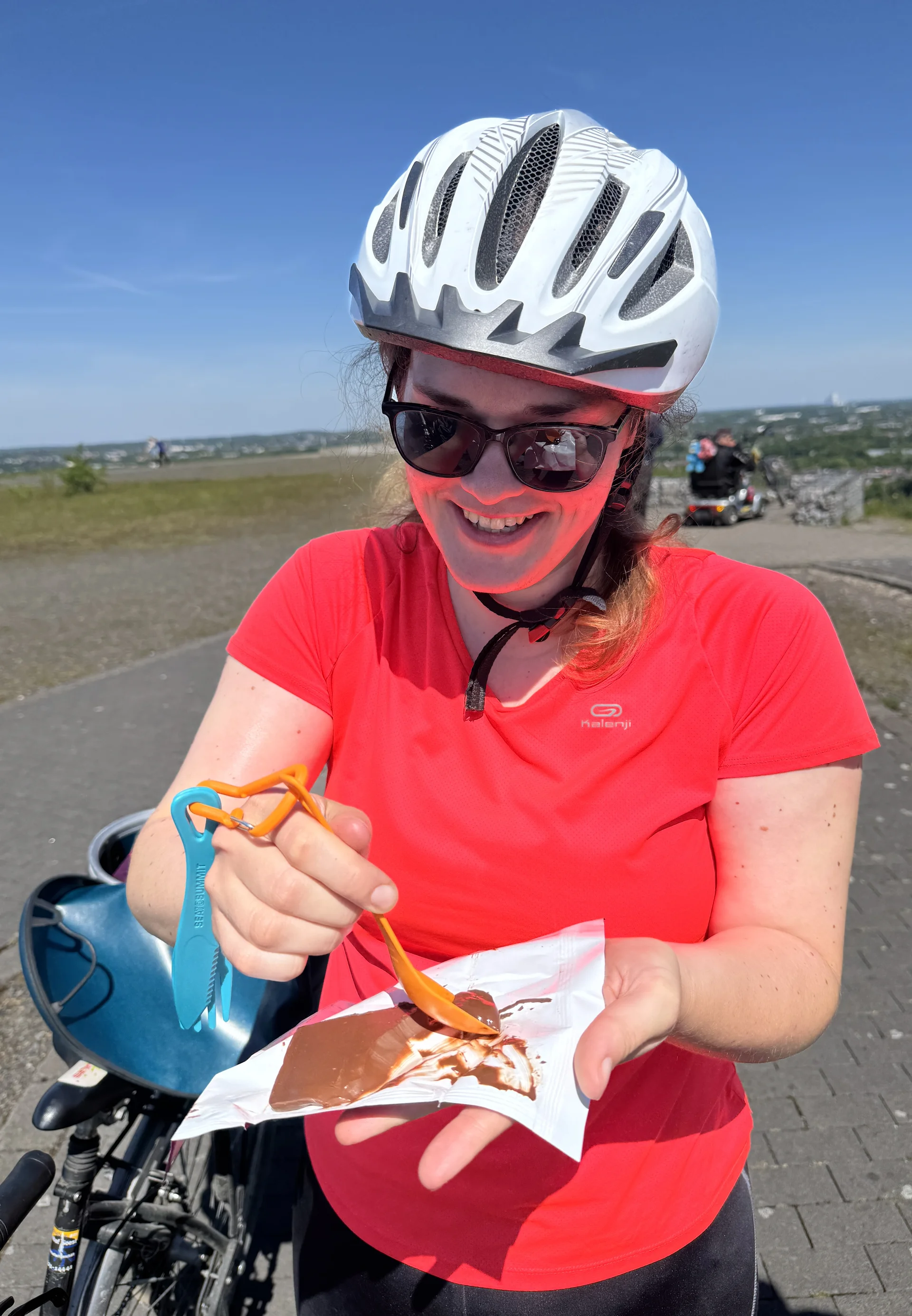 Frau mit Helm und Sonnenbrille isst Schokolade mit Gabel während einer Radtour. | © DAV Dortmund