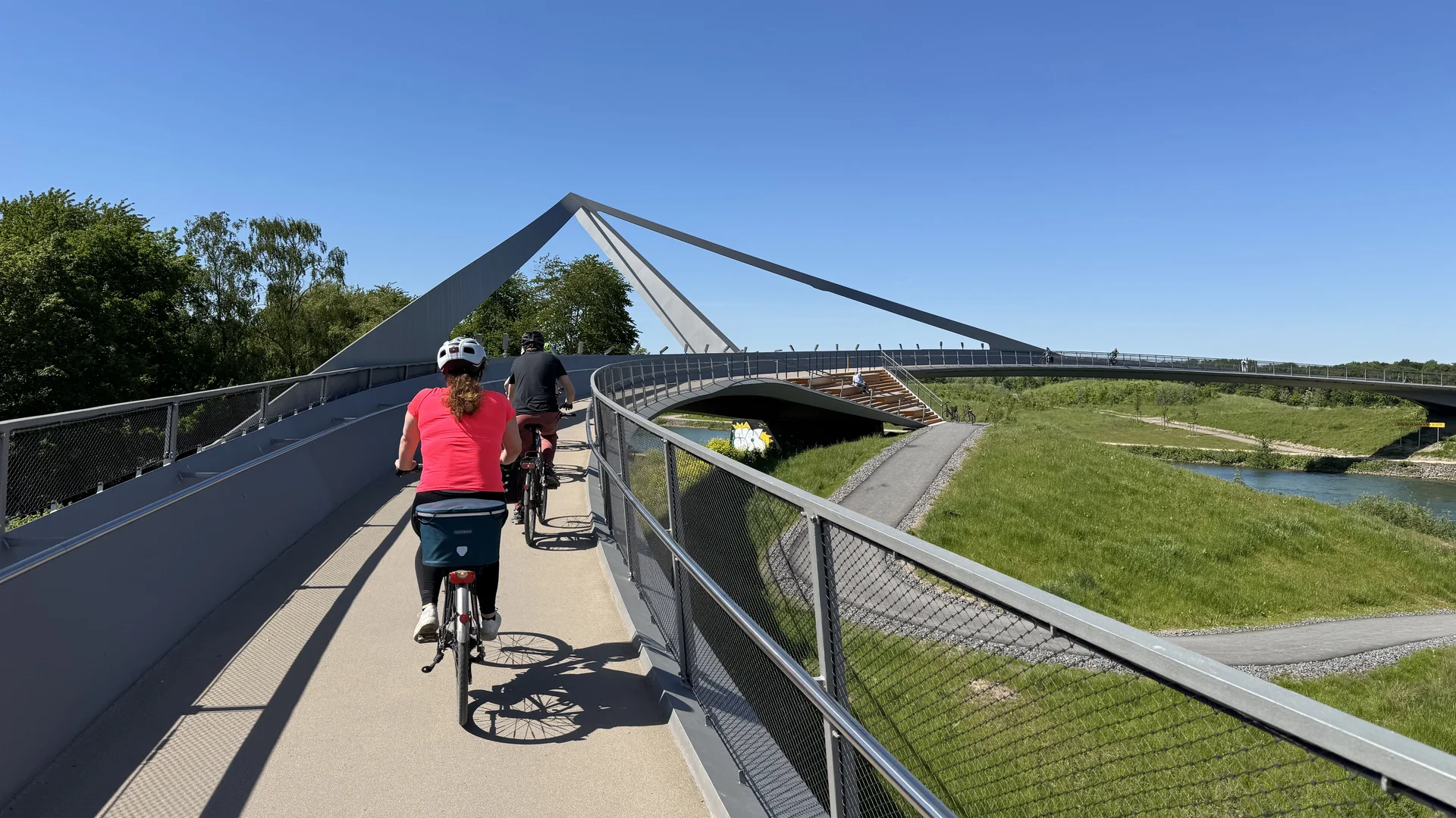 Radfahrer*innen überqueren eine moderne Brücke mit markanter Konstruktion und Geländern. | © DAV Dortmund