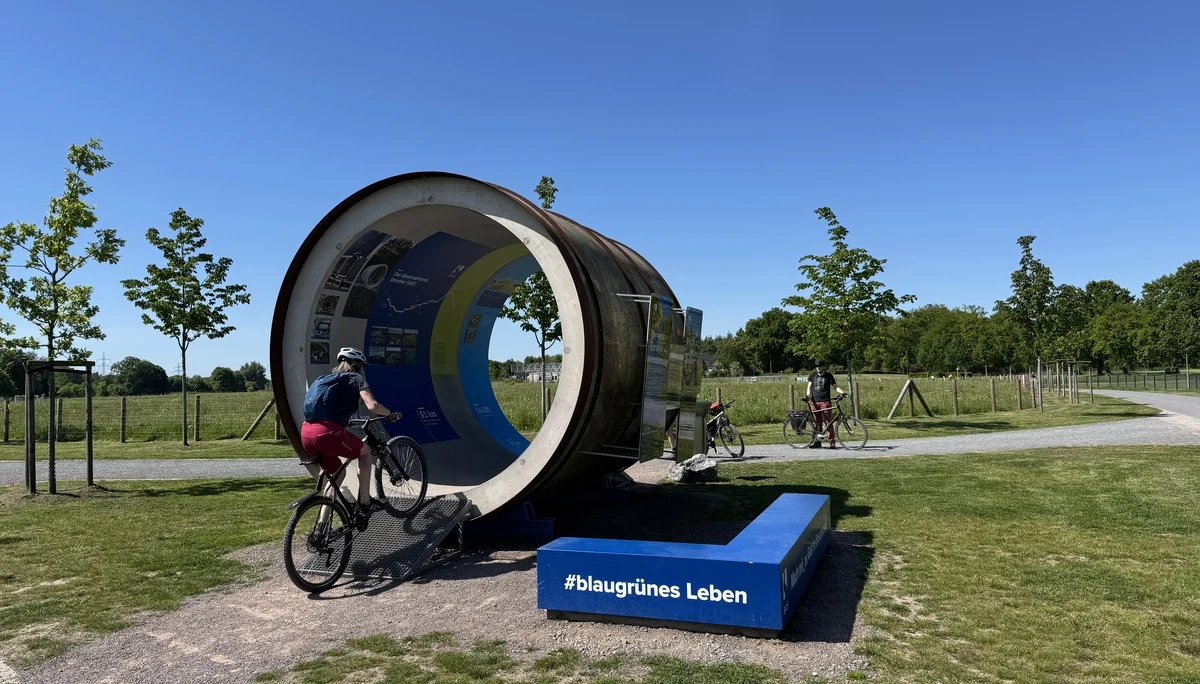 Radfahrer*innen fahren durch eine runde, künstlerische Tunnelkonstruktion mit Infotafeln. | © DAV Dortmund