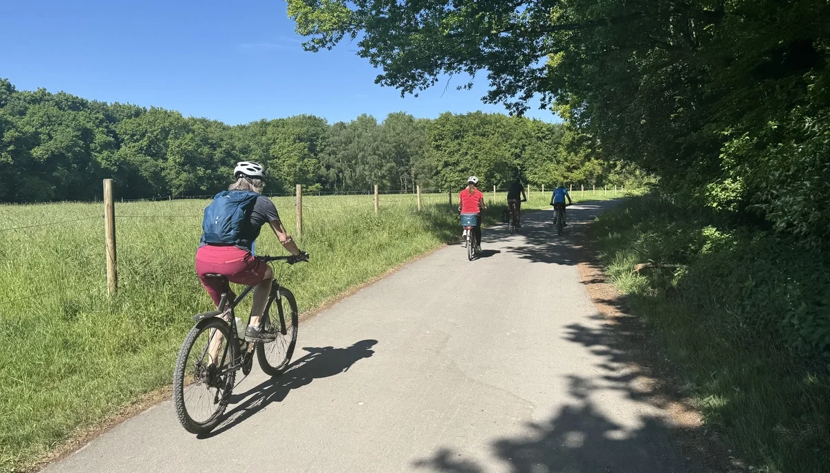 Mehrere Radfahrer*innen fahren bei Sonnenschein auf einem asphaltierten Weg neben einer Wiese. | © DAV Dortmund