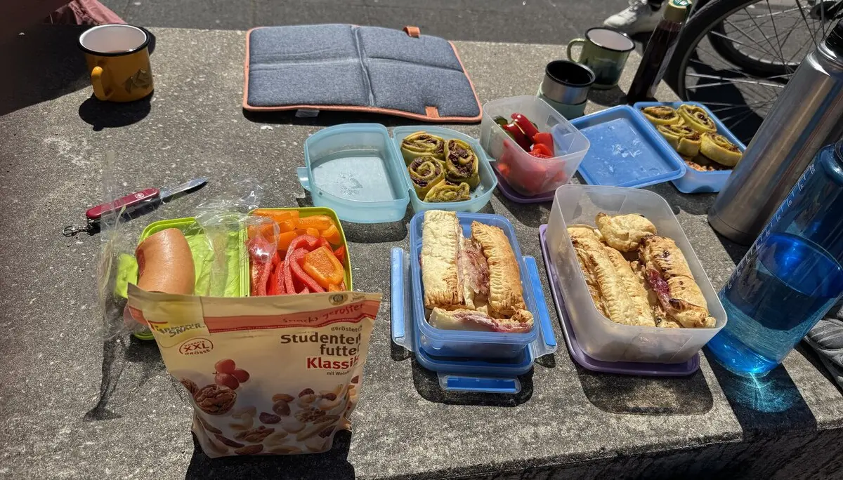 Verschiedene Brotboxen mit belegten Brötchen, Gemüse und Snacks auf einem Betonsockel im Freien. | © DAV Dortmund