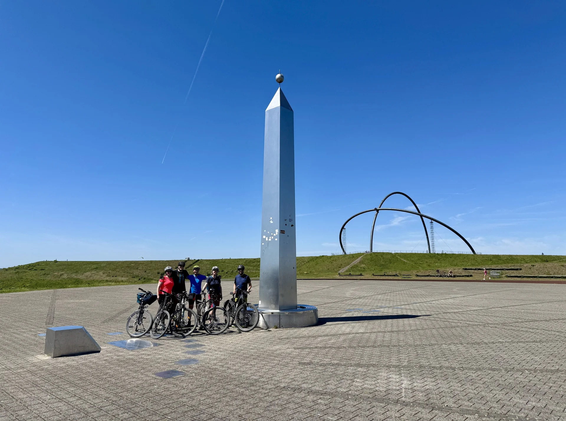 Fünf Radfahrer*innen stehen mit ihren Fahrrädern vor einem großen silbernen Obelisken und Kunstobjekt. | © DAV Dortmund