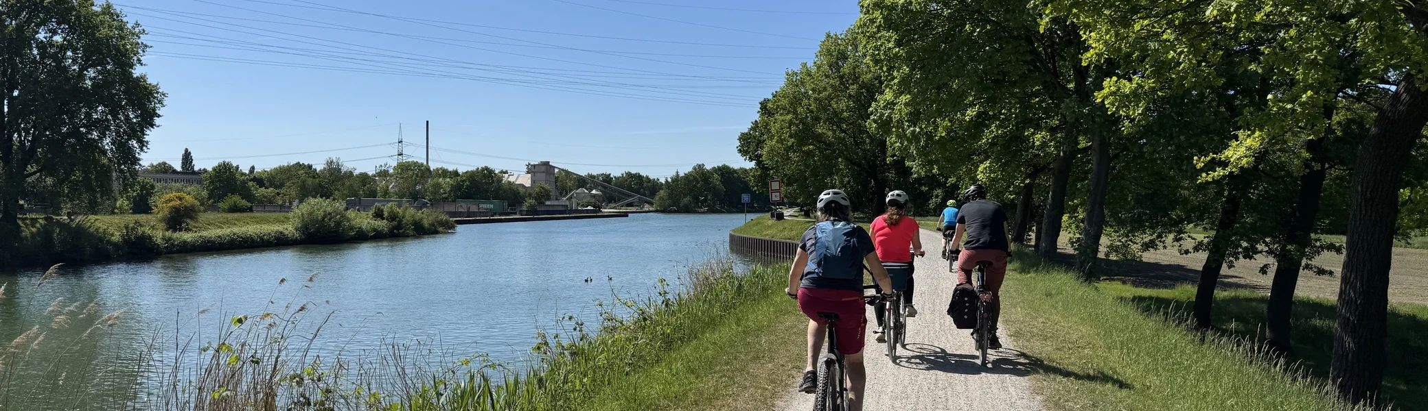 Gruppe radelt auf einem Schotterweg direkt am Wasser unter grünem Blätterdach. | © DAV Dortmund