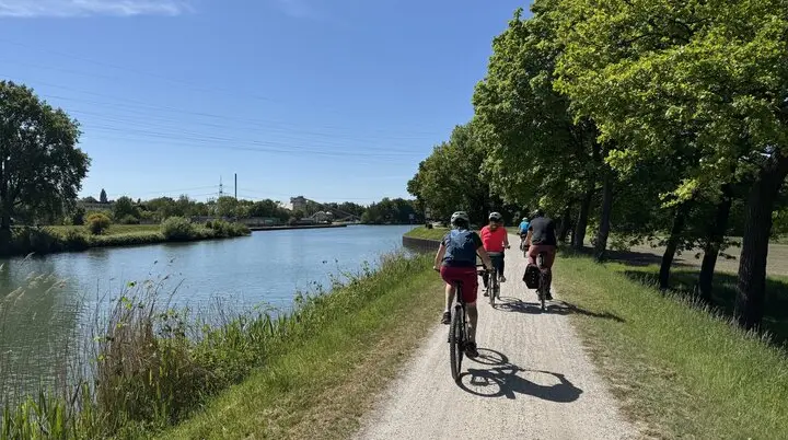 Gruppe radelt auf einem Schotterweg direkt am Wasser unter grünem Blätterdach. | © DAV Dortmund