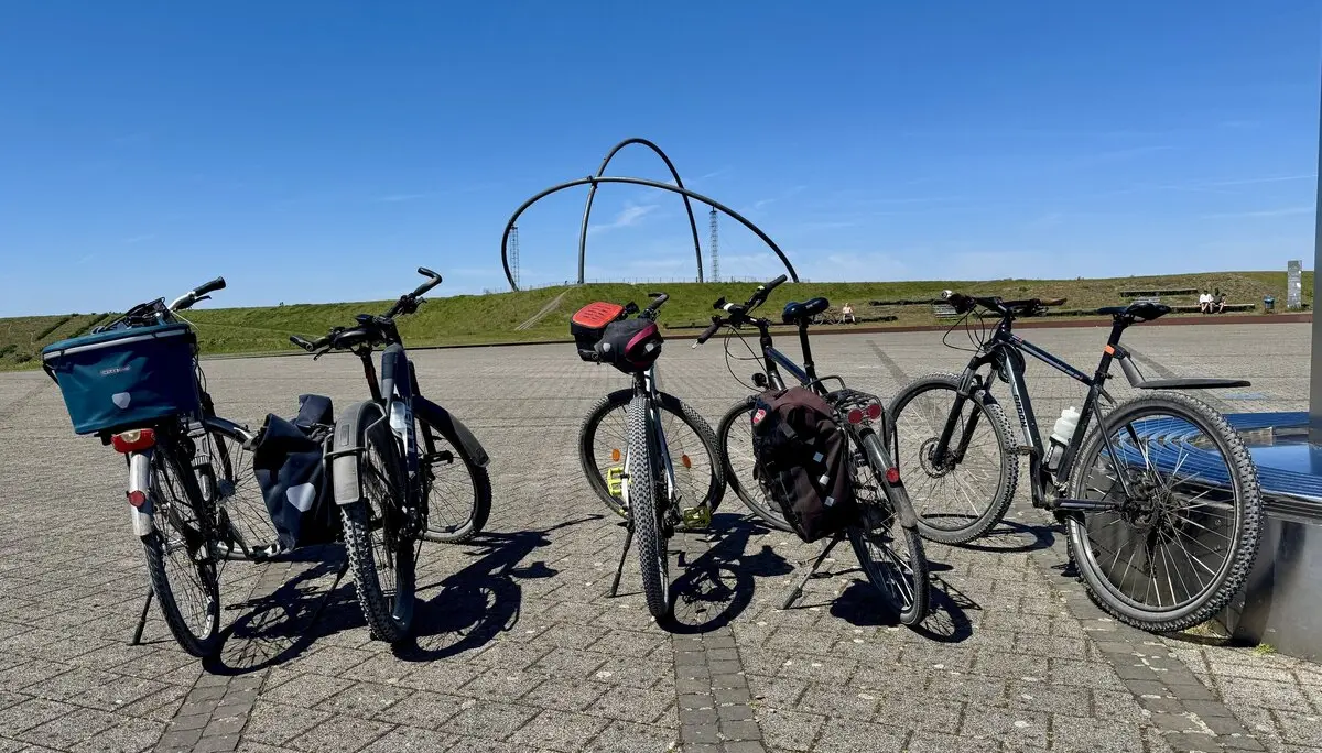Fünf abgestellte Fahrräder auf einem Platz mit moderner Skulptur im Hintergrund bei klarem Himmel. | © DAV Dortmund