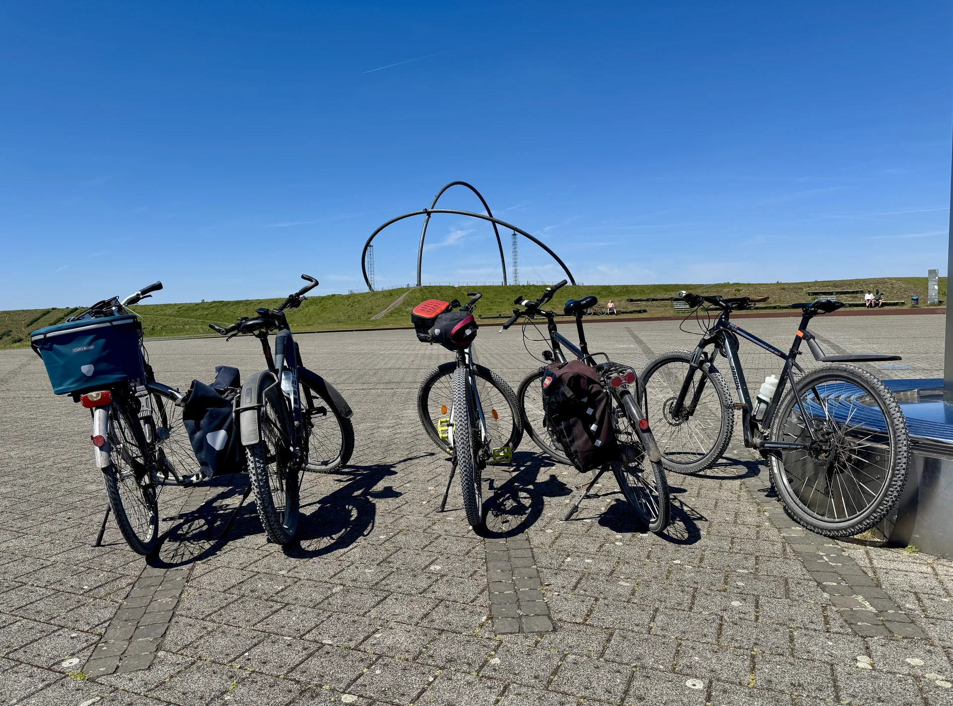 Fünf abgestellte Fahrräder auf einem Platz mit moderner Skulptur im Hintergrund bei klarem Himmel. | © DAV Dortmund