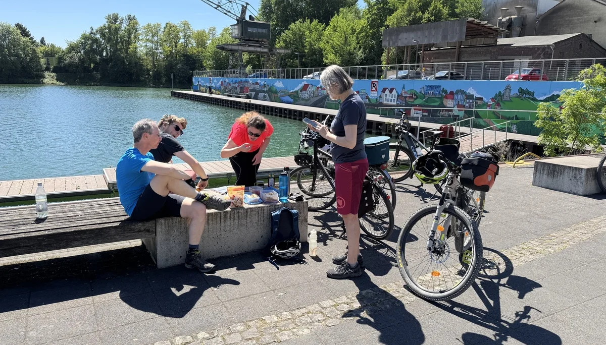 Vier Personen mit Fahrrädern sitzen und stehen an einem Ufer, essen und trinken bei Sonnenschein. | © DAV Dortmund