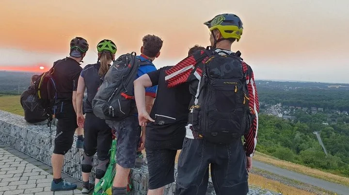 Mountainbiker*innen stehen auf einer Halde und schauen dem Sonnenuntergang entgegen. | © DAV Dortmund