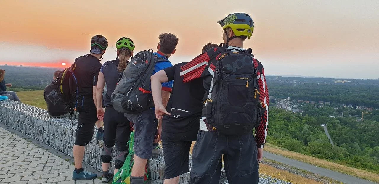 Mountainbiker*innen stehen auf einer Halde und schauen dem Sonnenuntergang entgegen. | © DAV Dortmund