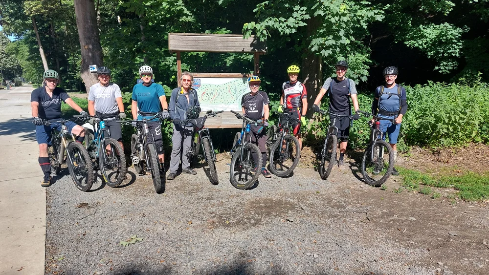 Acht Mountainbiker stehen mit ihren Rädern vor einer großen Karte im Waldgebiet, bereit zur gemeinsamen Tour. | © DAV Dortmund