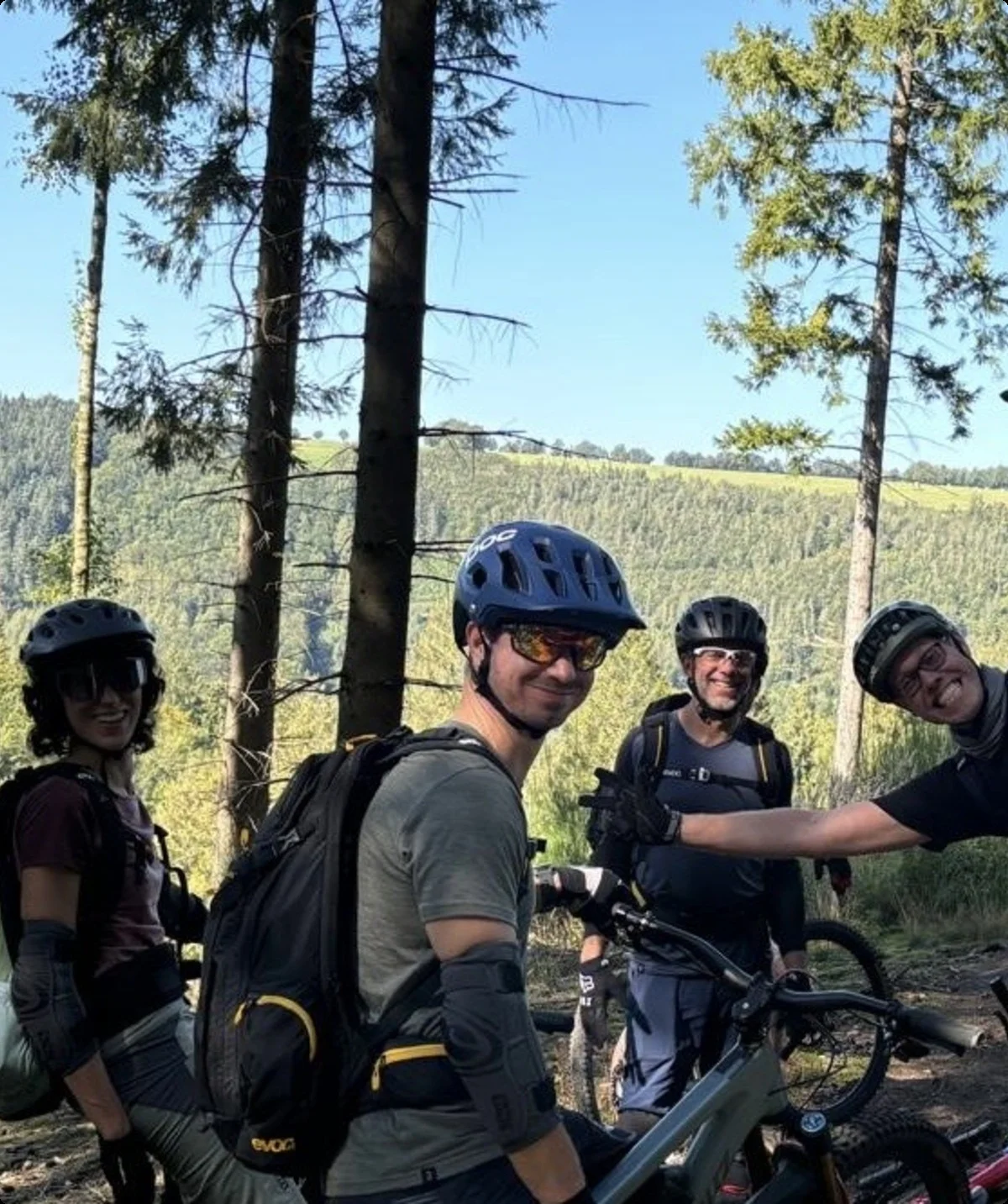 Eine Gruppe von Mountainbiker*innen macht eine Pause auf einem Waldweg, im Hintergrund grüne Hügel. | © DAV Dortmund