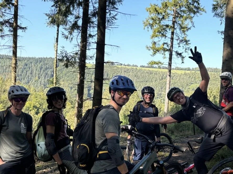 Eine Gruppe von Mountainbiker*innen macht eine Pause auf einem Waldweg, im Hintergrund grüne Hügel. | © DAV Dortmund