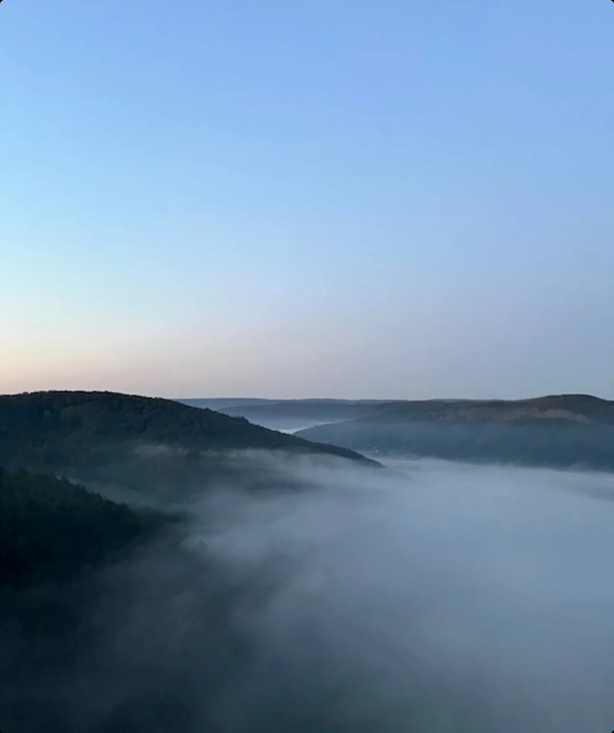 Eine ruhige Landschaft mit Hügeln, die von Frühnebel bedeckt sind, unter einem klaren Himmel. | © DAV Dortmund
