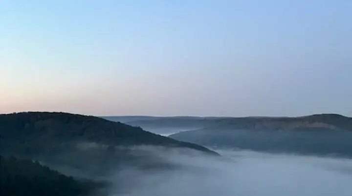 Eine ruhige Landschaft mit Hügeln, die von Frühnebel bedeckt sind, unter einem klaren Himmel. | © DAV Dortmund