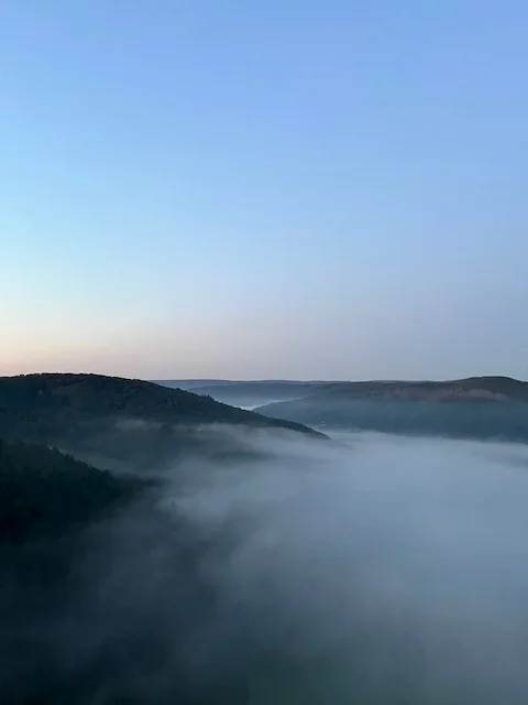 Eine ruhige Landschaft mit Hügeln, die von Frühnebel bedeckt sind, unter einem klaren Himmel. | © DAV Dortmund