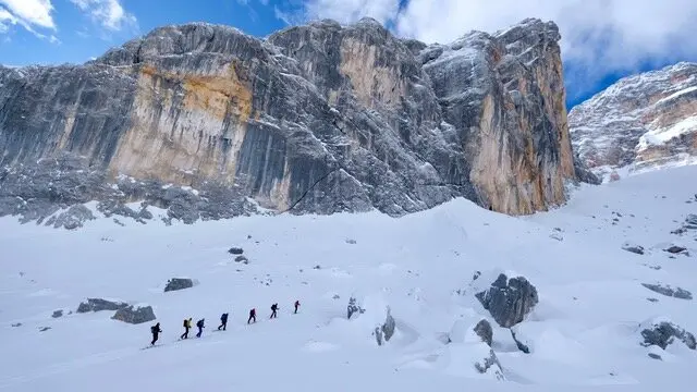 Eine Gruppe Skitourengeher*innen geht durch tiefen Schnee in einer spektakulären Winterlandschaft mit hohen Felsen. | © DAV Dortmund