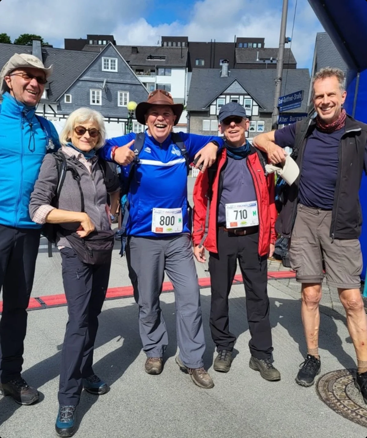 Fünf Personen stehen nach einem Wanderlauf unter dem Zieleinlaufbogen, einige tragen Startnummern und Wanderkleidung. | © DAV Dortmund