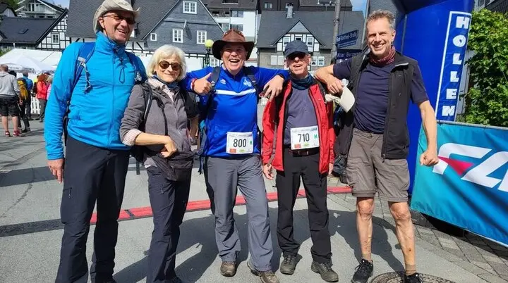 Fünf Personen stehen nach einem Wanderlauf unter dem Zieleinlaufbogen, einige tragen Startnummern und Wanderkleidung. | © DAV Dortmund