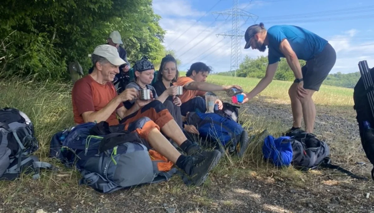 Eine Gruppe von Wandernden sitzt am Waldrand unter einem Baum im Schatten. Sie trinken aus Bechern und entspannen sich auf ihren Rucksäcken. | © DAV Dortmund