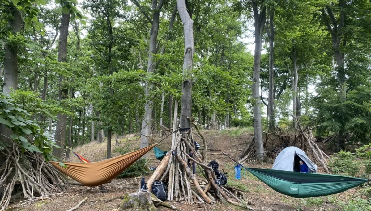Zwei Hängematten und ein Zelt sind zwischen Bäumen im Wald aufgebaut. Rundherum stehen improvisierte Unterstände aus Ästen und mehrere Rucksäcke. | © DAV Dortmund