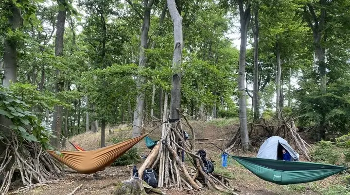 Zwei Hängematten und ein Zelt sind zwischen Bäumen im Wald aufgebaut. Rundherum stehen improvisierte Unterstände aus Ästen und mehrere Rucksäcke. | © DAV Dortmund