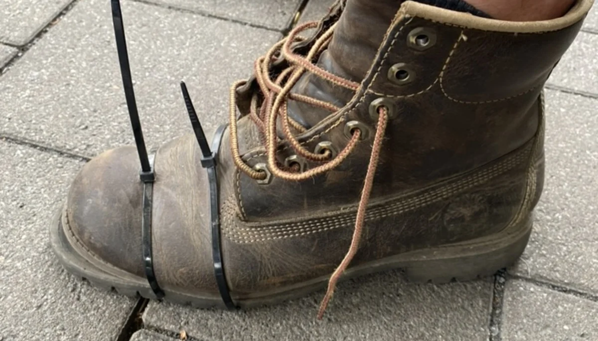 Ein robuster Wanderschuh ist mit zwei Kabelbindern an der Spitze repariert. Der Schuh steht auf einem gepflasterten Untergrund. | © DAV Dortmund