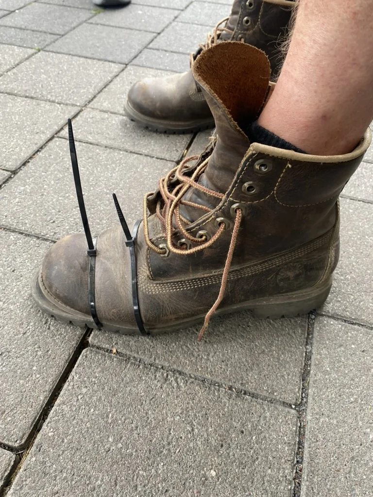 Ein robuster Wanderschuh ist mit zwei Kabelbindern an der Spitze repariert. Der Schuh steht auf einem gepflasterten Untergrund. | © DAV Dortmund