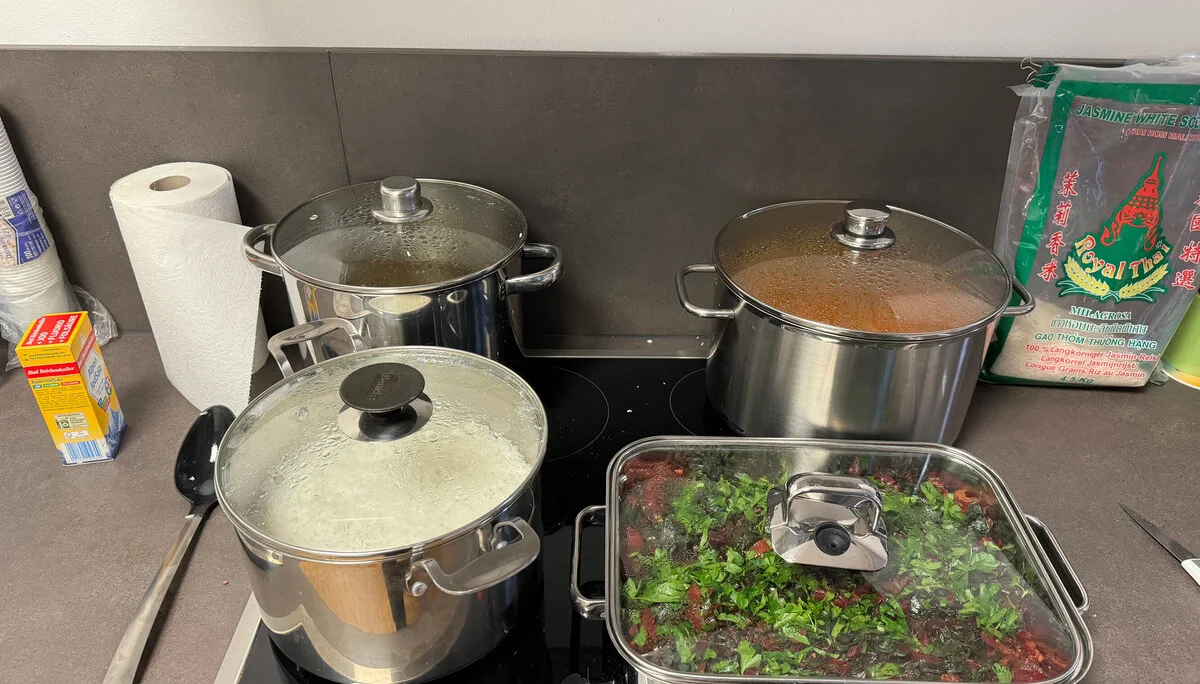 Vier Töpfe und Pfannen stehen auf einem Herd. Es wird gekocht, Gemüse ist sichtbar, daneben stehen Küchentücher, Gewürze und eine Packung Reis. | © DAV Dortmund