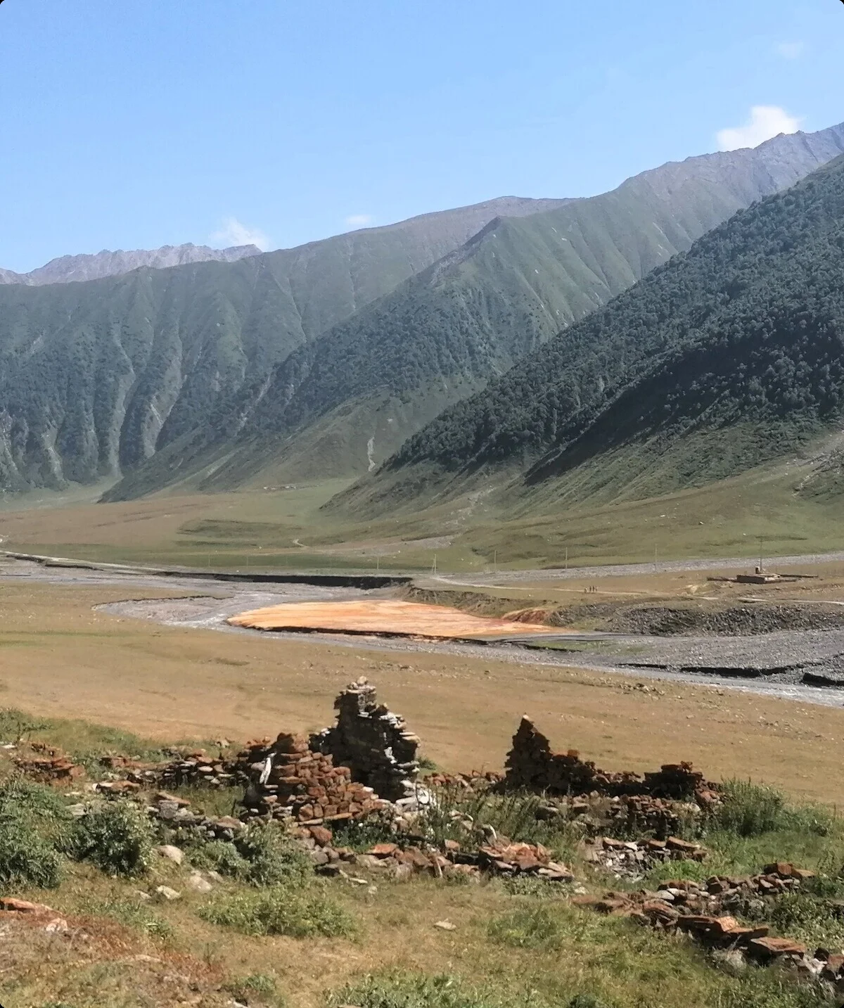 Ein alter Steinturm steht in einem weiten Tal mit Ruinenresten, umgeben von grünen Berghängen | © DAV Dortmund