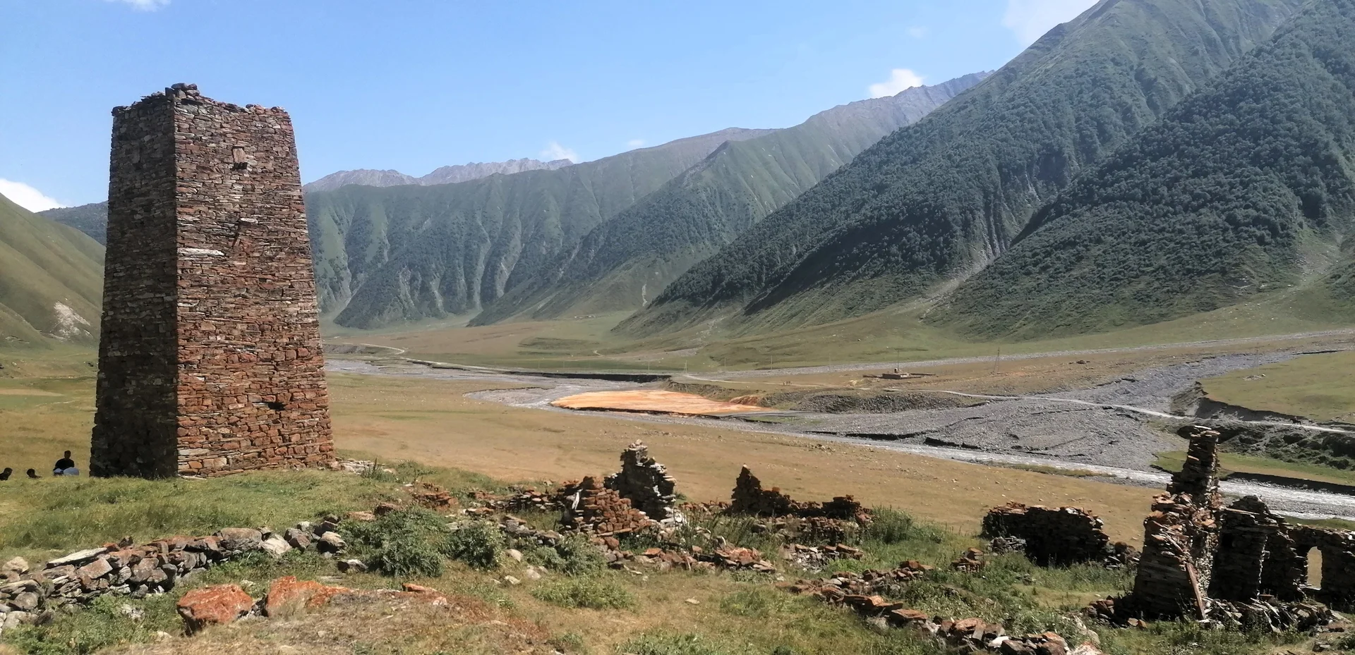 Ein alter Steinturm steht in einem weiten Tal mit Ruinenresten, umgeben von grünen Berghängen | © DAV Dortmund