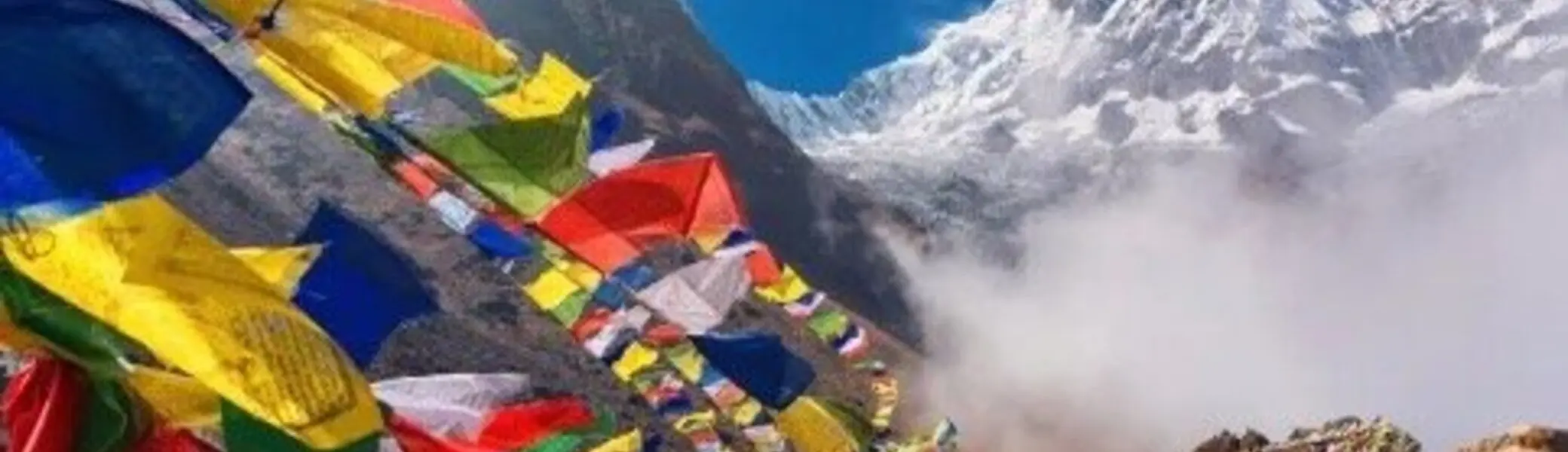 Bunte tibetische Gebetsfahnen flattern im Wind vor einer beeindruckenden Berglandschaft mit Schnee und Nebel | © DAV Dortmund