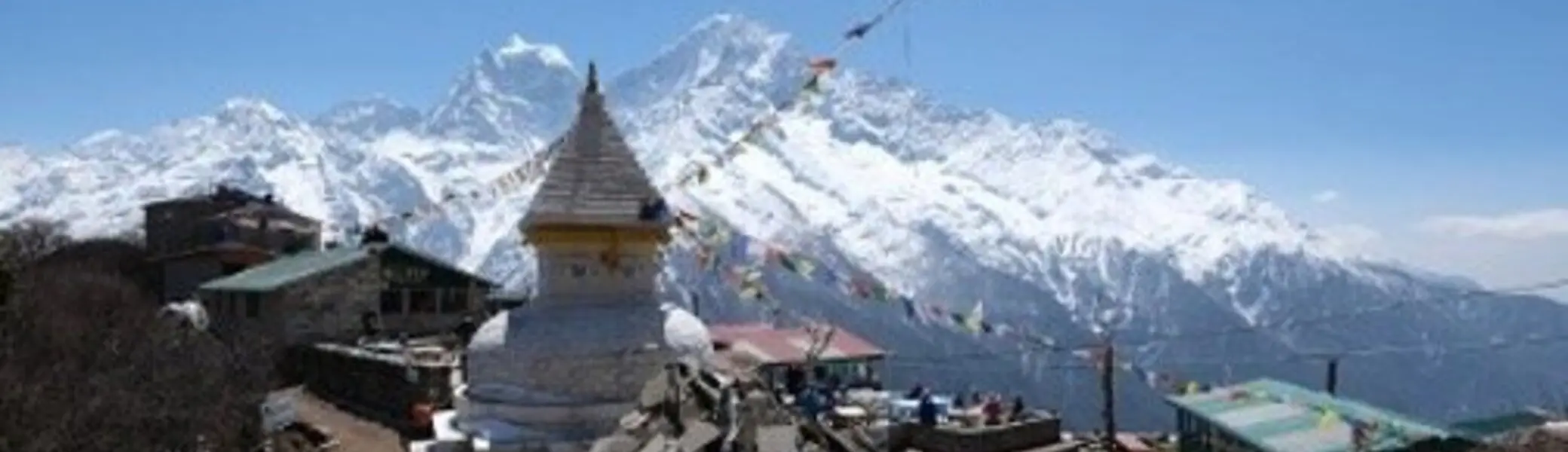 Ein weißer Stupa mit goldener Spitze steht im Vordergrund, dahinter Häuser, Gebetsfahnen und die schneebedeckten Gipfel des Himalaya | © DAV Dortmund
