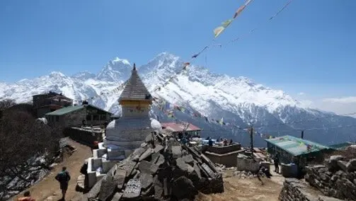 Ein weißer Stupa mit goldener Spitze steht im Vordergrund, dahinter Häuser, Gebetsfahnen und die schneebedeckten Gipfel des Himalaya | © DAV Dortmund