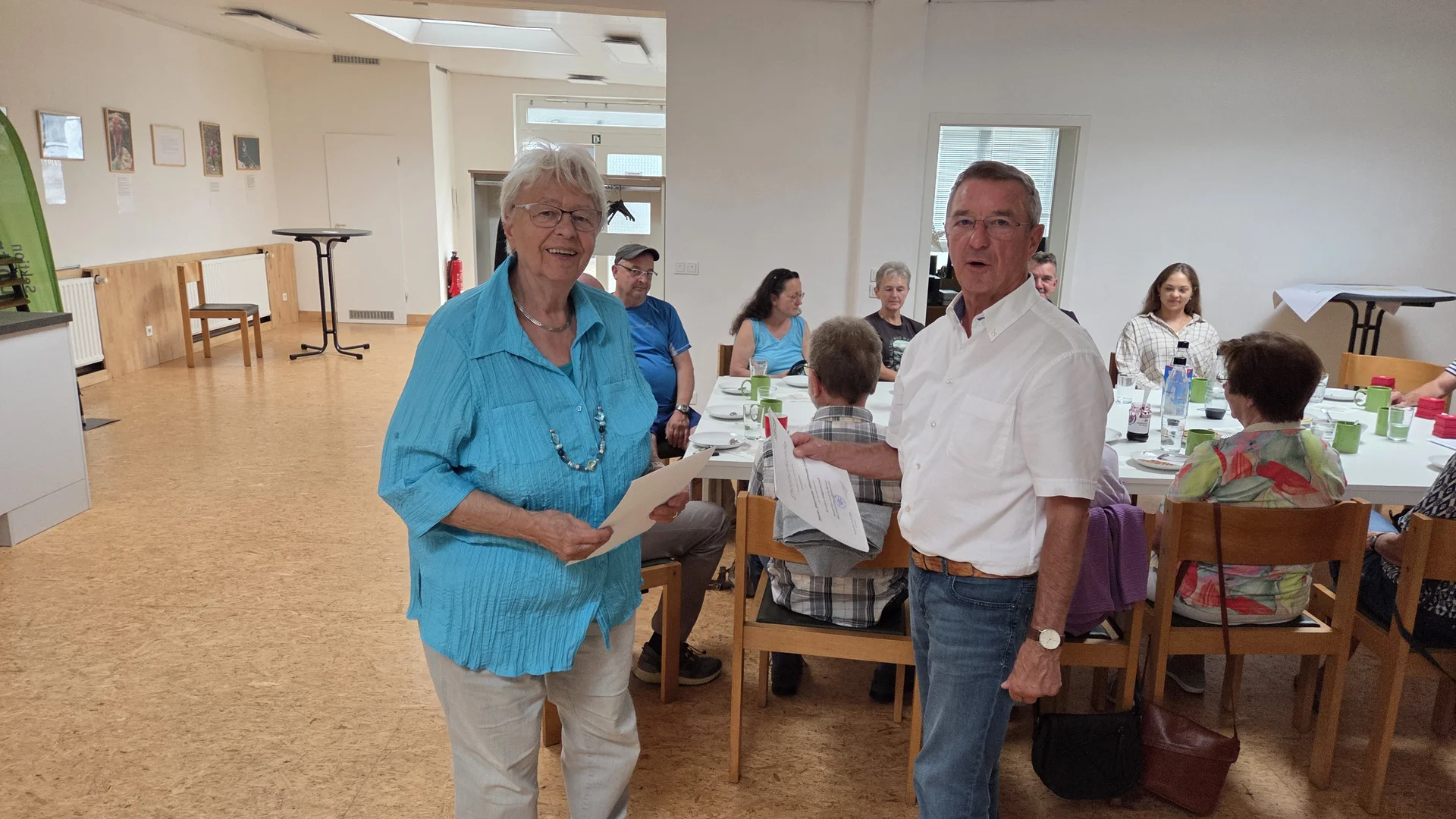 Frau Hein erhält ihre Urkunde, im Hintergrund sitzen weitere Mitglieder der DAV Sektion Dortmund und beobachten die Übergabe. | © DAV Dortmund