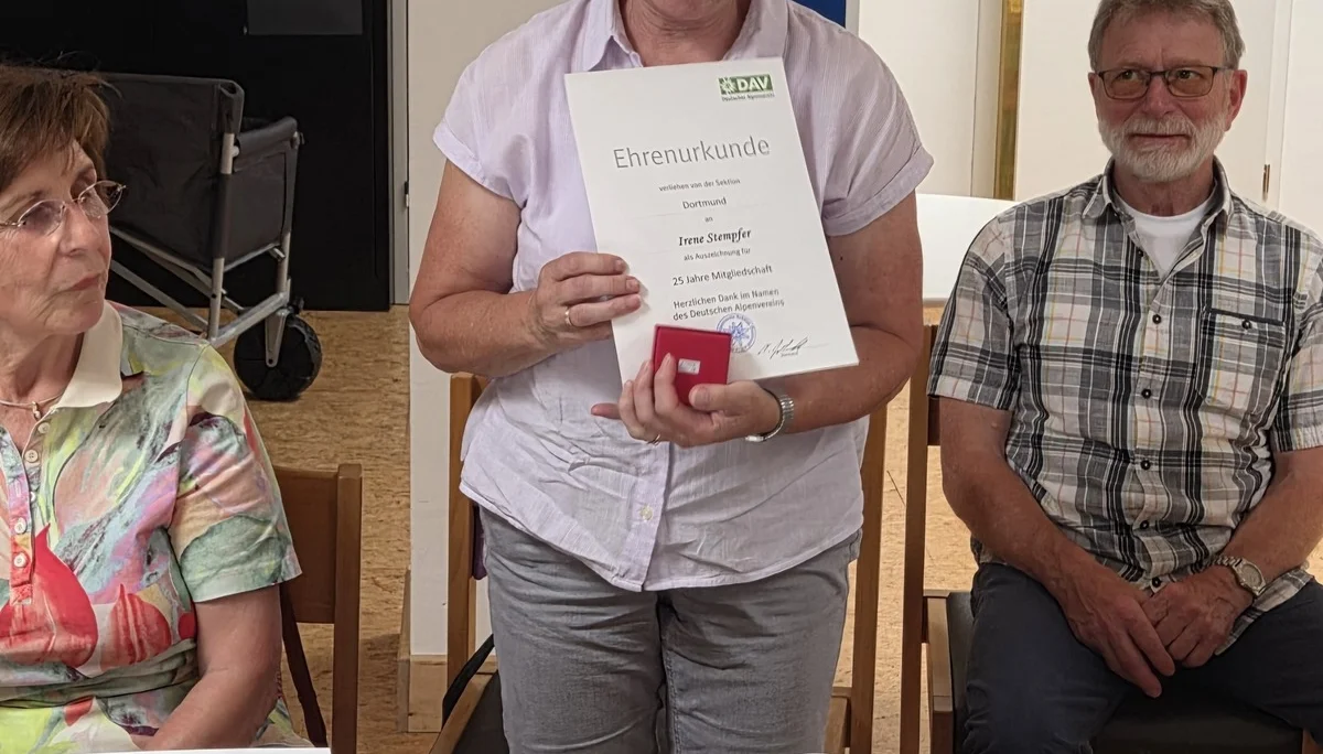 Irene zeigt ihre Ehrenurkunde für 25 Jahre Mitgliedschaft in der DAV Sektion Dortmund und hält eine kleine rote Schachtel in der Hand. | © DAV Dortmund