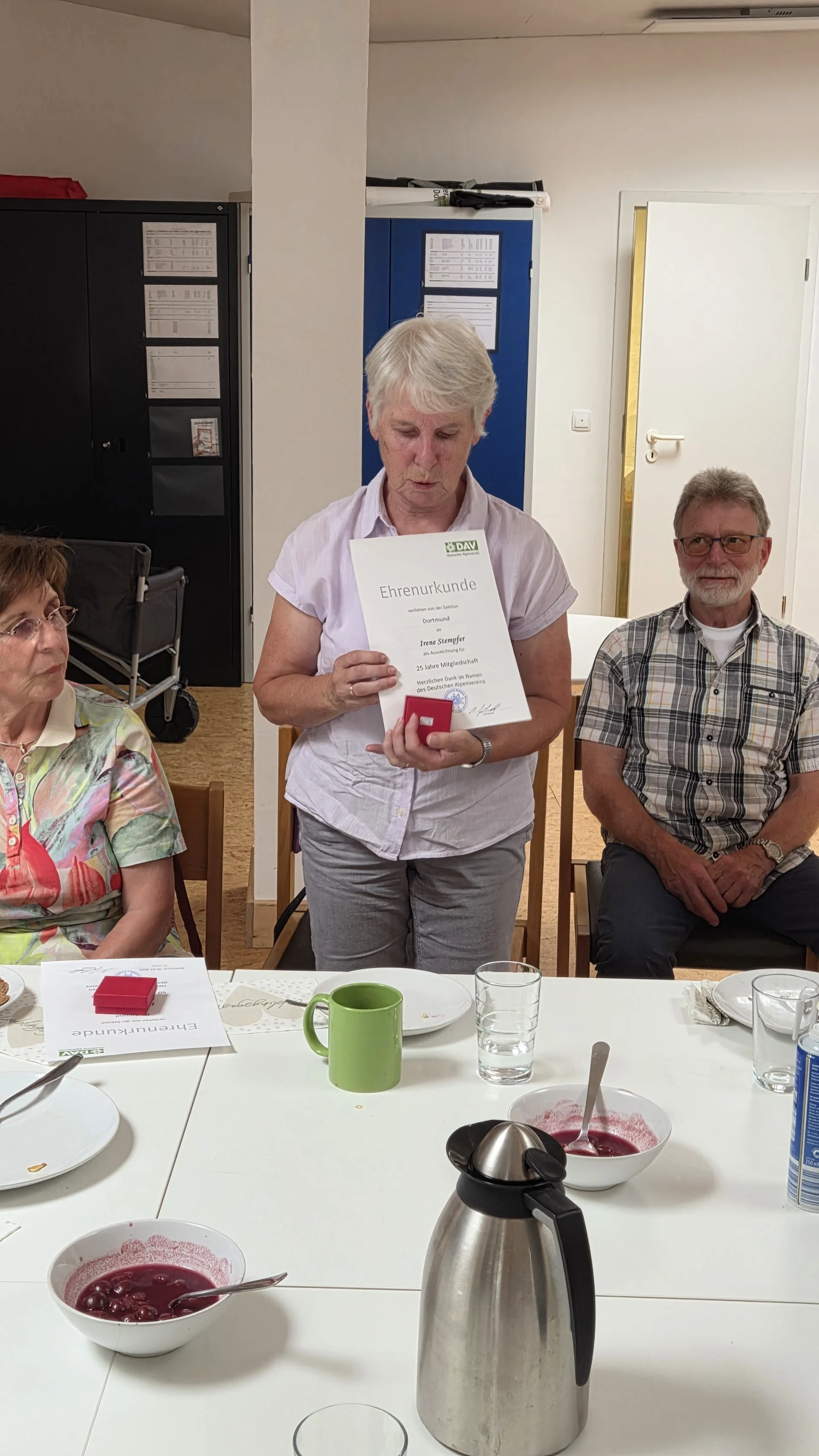 Irene zeigt ihre Ehrenurkunde für 25 Jahre Mitgliedschaft in der DAV Sektion Dortmund und hält eine kleine rote Schachtel in der Hand. | © DAV Dortmund