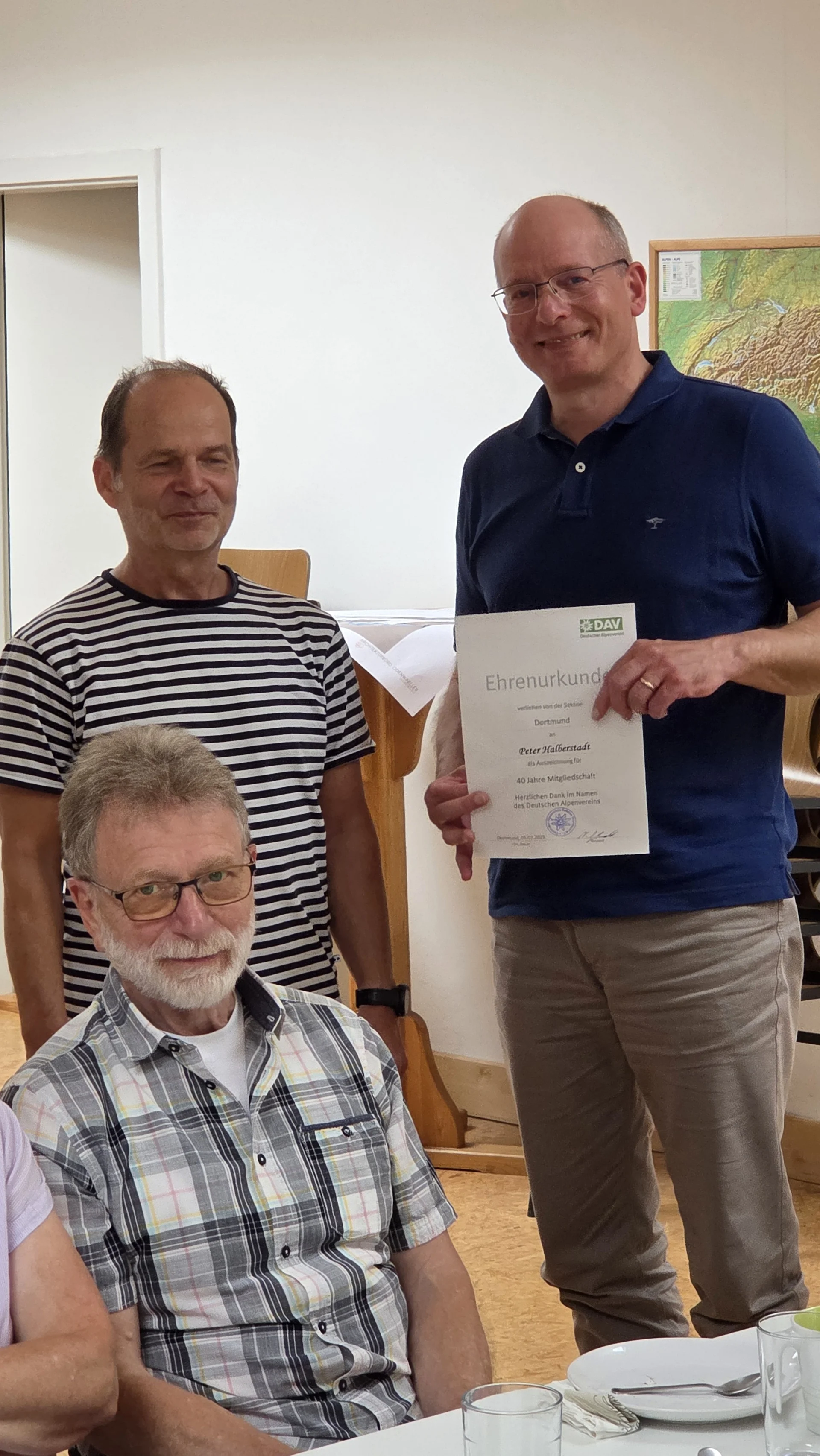 Peter bekommt eine Urkunde für 40 Jahre Mitgliedschaft bei der DAV Sektion Dortmund, daneben stehen Peter und ein weitere Mitglieder. | © DAV Dortmund