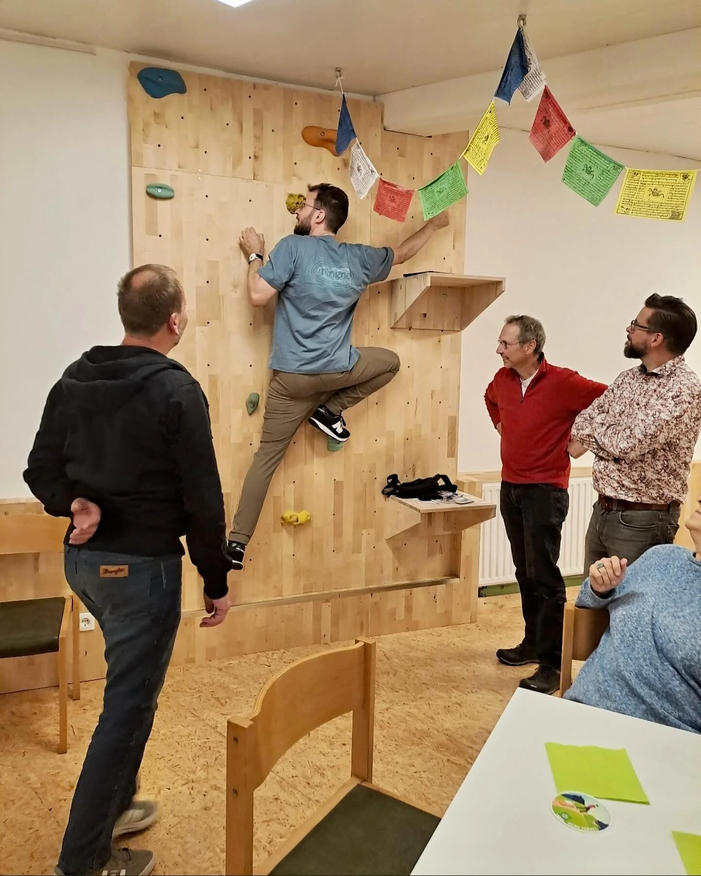 Eine Person klettert an einer Holzwand mit Griffen, umgeben von anderen Personen, die zuschauen. | © DAV Dortmund